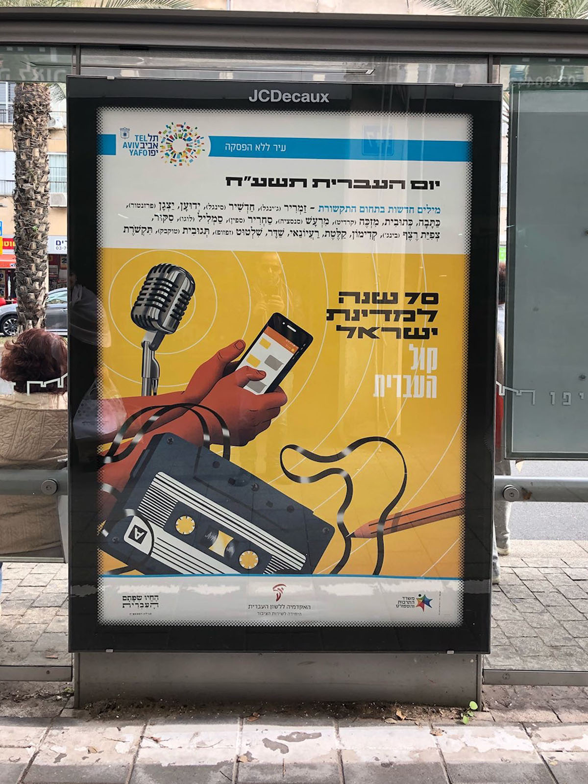 צילום כרזה ליום העברית תשע"ח איור של קלטת, מיקרופון וטלפון סלולרי וכיתוב "קול העברית"